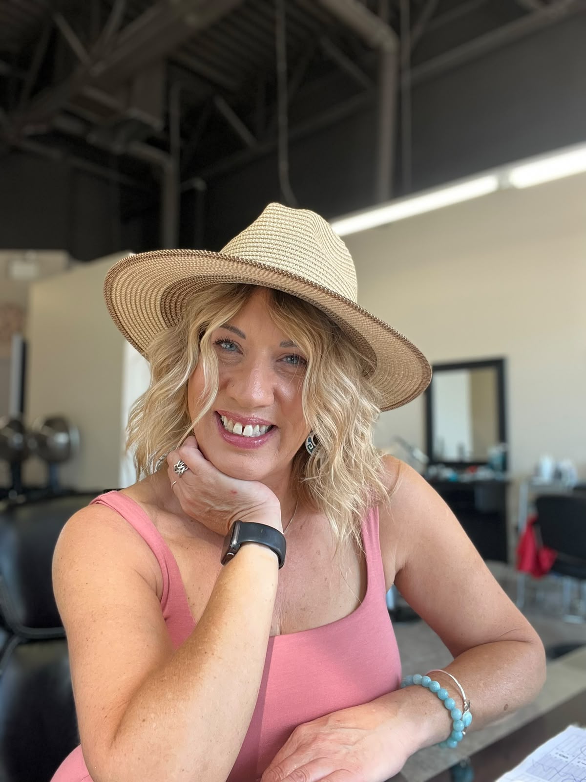 Kelly May smiling in her salon, wearing a straw hat